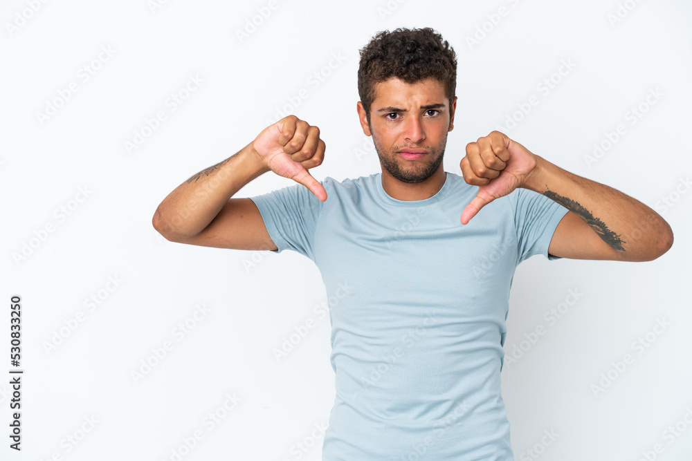 Young handsome Brazilian man isolated on white background showing thumb down with two hands Young handsome Brazilian man isolated on white background showing thumb down with two hands
