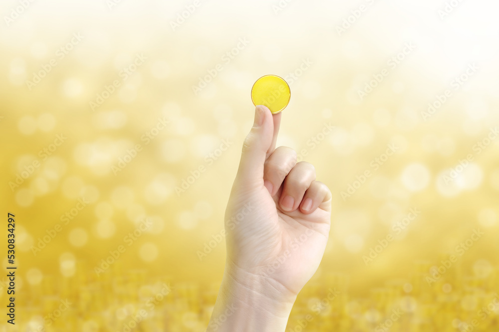 gold coin holding gold coin in hand on a blurred golden yellow bokeh background.