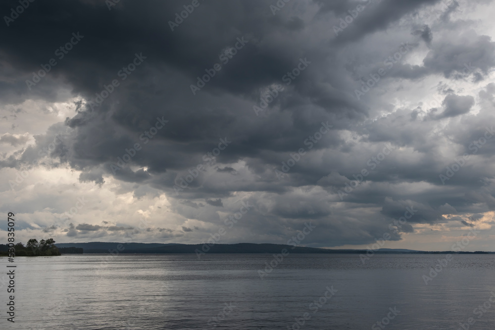 Naklejka premium Dark heavy thunderstorm clouds over a lake surface. Thunder storm, active weather concept.