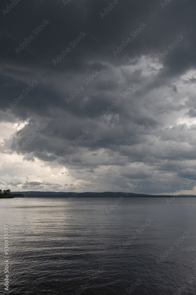 Fototapeta premium Dark heavy thunderstorm clouds over a lake surface. Thunder storm, active weather concept.