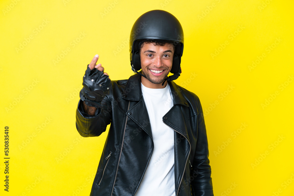 Young Brazilian man with a motorcycle helmet isolated on yellow background doing coming gesture Young Brazilian man with a motorcycle helmet isolated on yellow background doing coming gesture