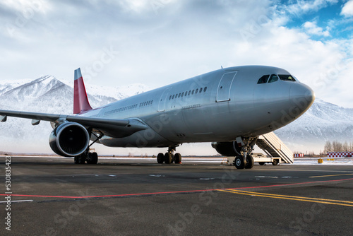 Wide body passenger jetliner and boarding stairs at the airport apron on the background of high scenic snow-capped mountains