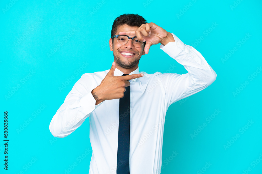 Young business Brazilian man isolated on blue background focusing face. Framing symbol Young business Brazilian man isolated on blue background focusing face. Framing symbol