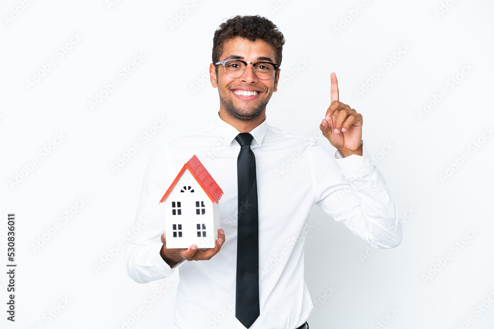 Young business Brazilian man holding a house toy isolated on white background pointing up a great idea Young business Brazilian man holding a house toy isolated on white background pointing up a great idea