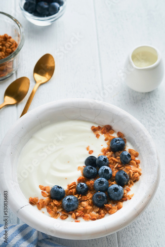 Yogurt. Greek Yogurt with granola and fresh blueberries in white bowl over old white wood background. Morning breakfast concept. Healthy food for breakfast, top view