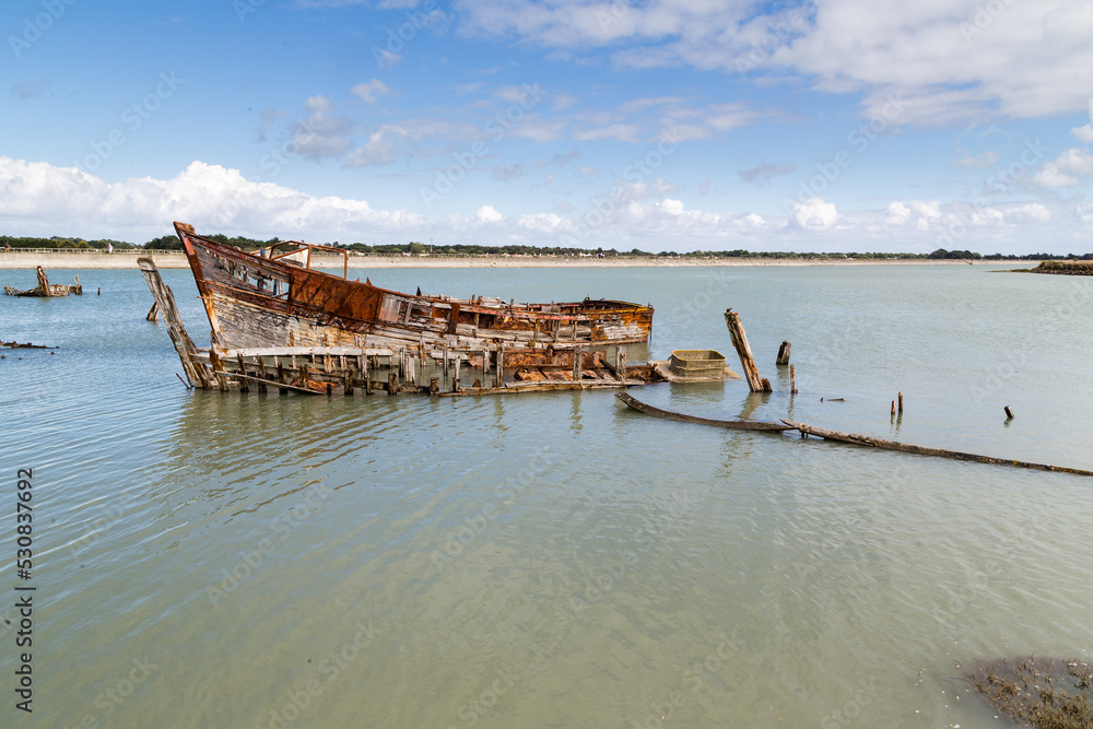 Cimetière de bateaux en bois dans un étier à marée haute derrière une jetée. Port de Noirmoutier