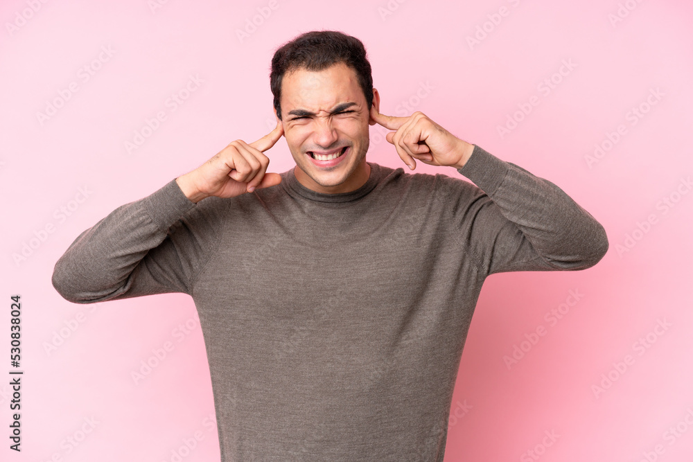 Young caucasian man isolated on pink background frustrated and covering ears