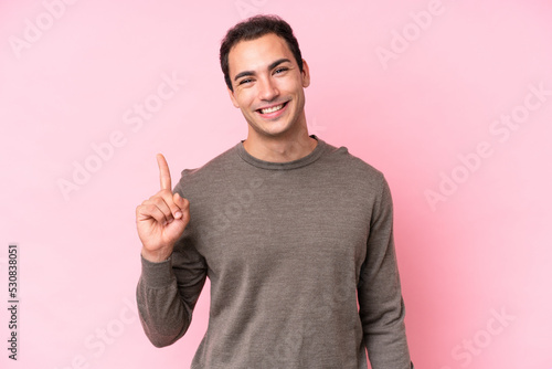 Young caucasian man isolated on pink background showing and lifting a finger in sign of the best