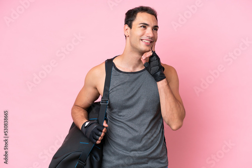 Young sport caucasian man with sport bag isolated on pink background thinking an idea while looking up