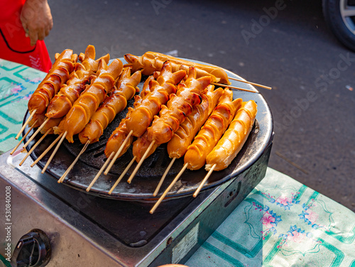 A number of sausage skewers grilled on a street food stall during a weekend bazaar.