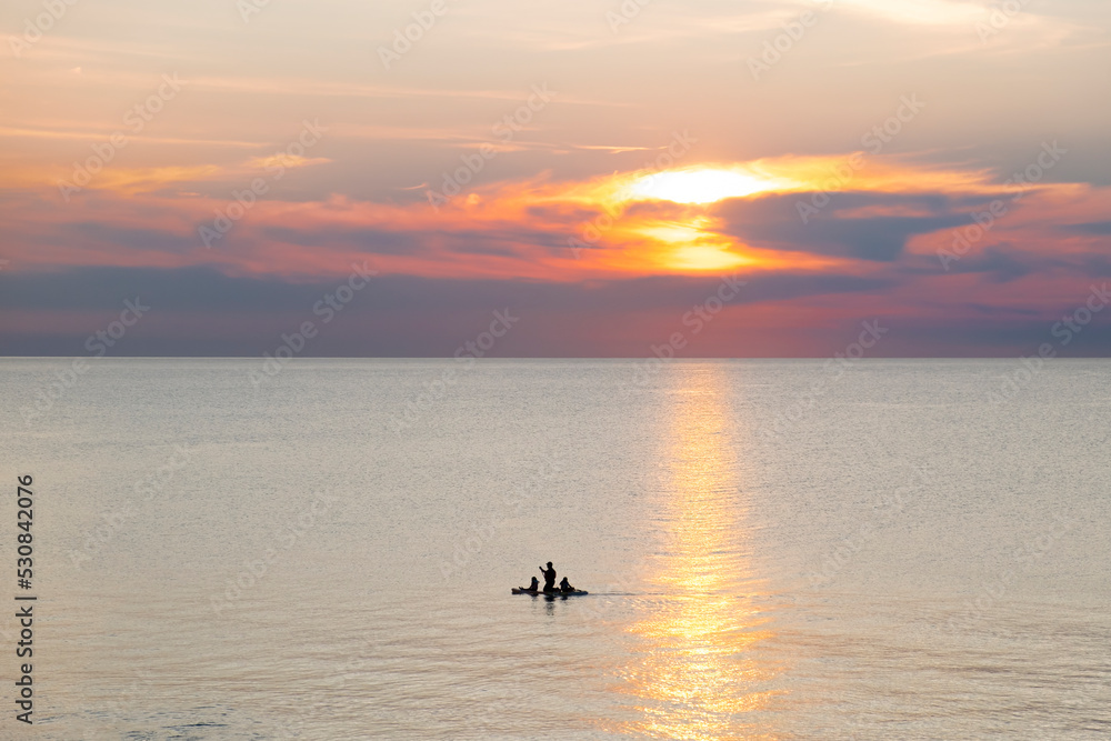 Obraz premium Silhouette of a man with two kids floating on a paddle boars in sunset hour. Pinery Provincial Park, Lake Huron, Ontario, Canada.