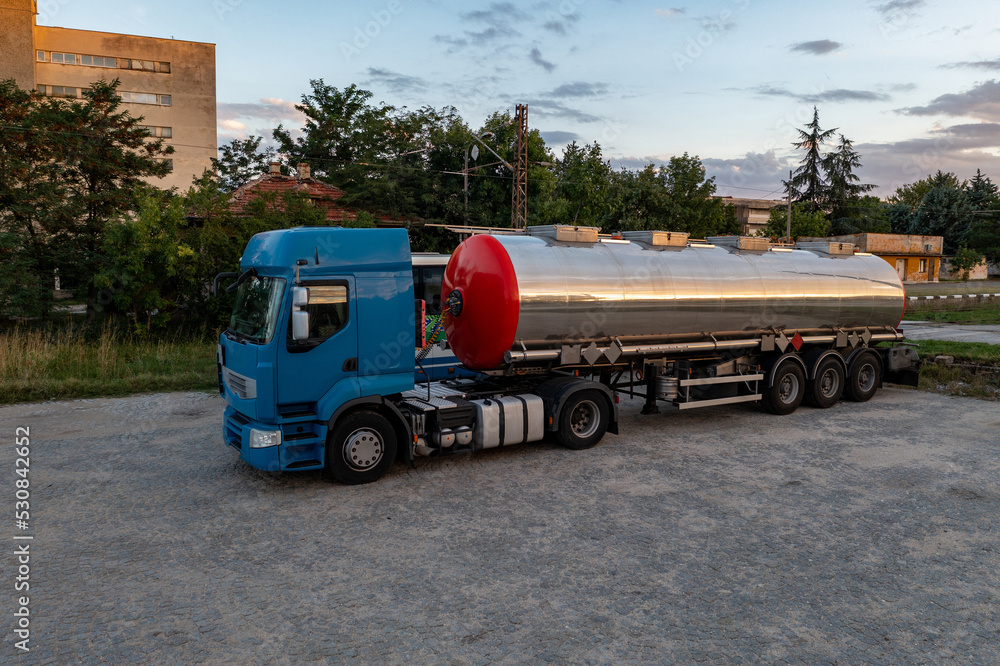 Big metal fuel tanker truck shipping fuel against a cloudy sky.