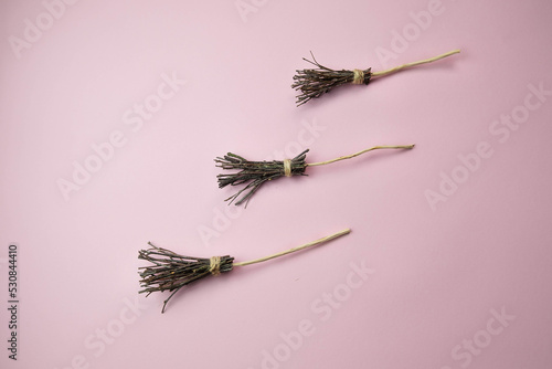 three witch brooms on a light pink background with a place for text, the concept of a creative happy Halloween
