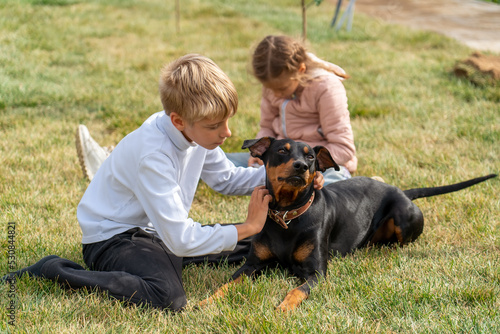 Teen boy hugging dog on lawn at backyard. School boy lovingly embraces his German Pinscher. Cute children with their pet summer outdoors.