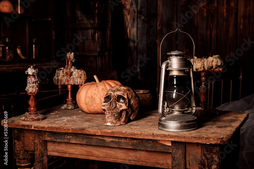 Photography On a wooden table lies a human skull, a pumpkin and a lamp