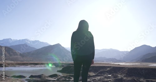A beautiful and young woman observing the horizon full of mountains and nature. You can see the silhouette with lensflares of the sun. Watching with peace. Concept of nature, introspection, meditation photo
