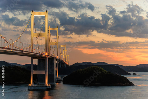 Lights from Kurushima Bridge mix with sunset glow over islands in Seto Inland Sea photo