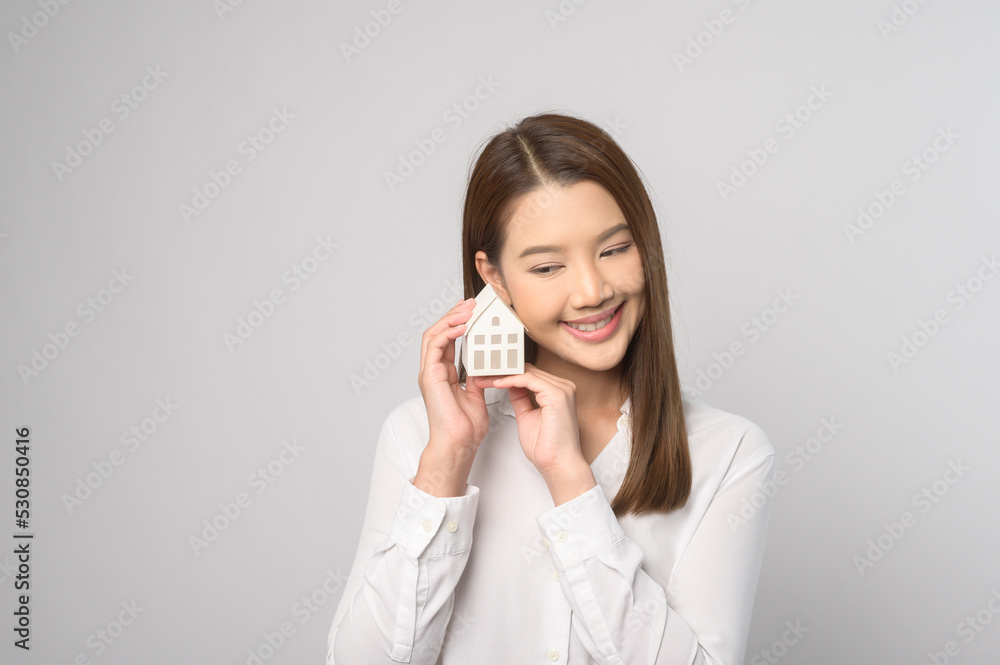 Young smiling woman holding small model house over white background studio. Young smiling woman holding small model house over white background studio.
