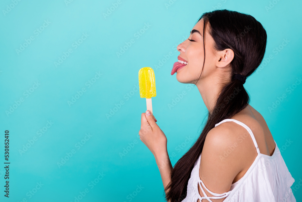 Profile side photo of cute pretty lady lick frozen tasty fruit popsicle isolated aquamarine color background Profile side photo of cute pretty lady lick frozen tasty fruit popsicle isolated aquamarine color background
