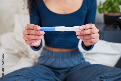 Close up of hands holding pregnancy test sitting on bed neutral result photo