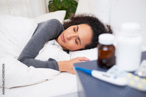 Tela A young multi-ethnic woman sleeps in bed recovering from flu with medication