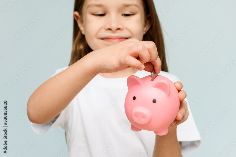 Smiling little girl posing with a piggy bank in her hands, standing against a blue background in a studio with free space. Family savings. Smiling little girl posing with a piggy bank in her hands, standing against a blue background in a studio with free space. Family savings.