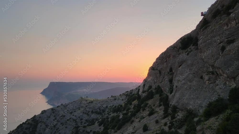Cinematic flight at sunset near a huge rock. The rays of the sun beautifully pass through the mountain covered with trees. Rocky sea coast . Cinematic flight at sunset near a huge rock. The rays of the sun beautifully pass through the mountain covered with trees. Rocky sea coast .
