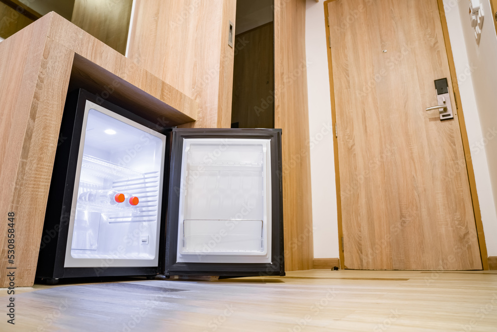 Small refrigerator under a wooden counter with two water bottles in a