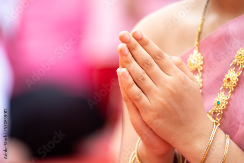 A Lady clasps her hands in front of her chest to pray. She wears .Thai traditional costume in Pink with golden traditional accessories, necklace and bracelets. . photo