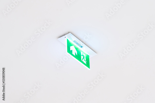 White neon sign depicting a fire exit with green background hangs from the ceiling.