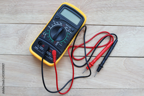 Digital multimeter with probes isolated on a wooden background closeup.