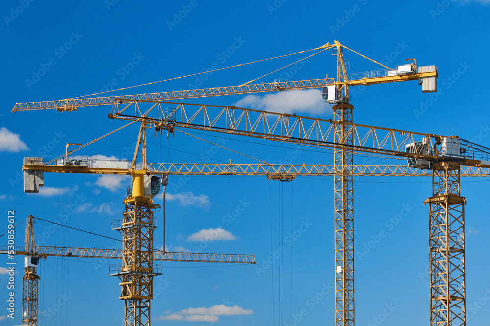 Cranes at construction site. Large construction site, cranes. Tower cranes in action on blue sky background. Housing renovation concept. Selective focus
