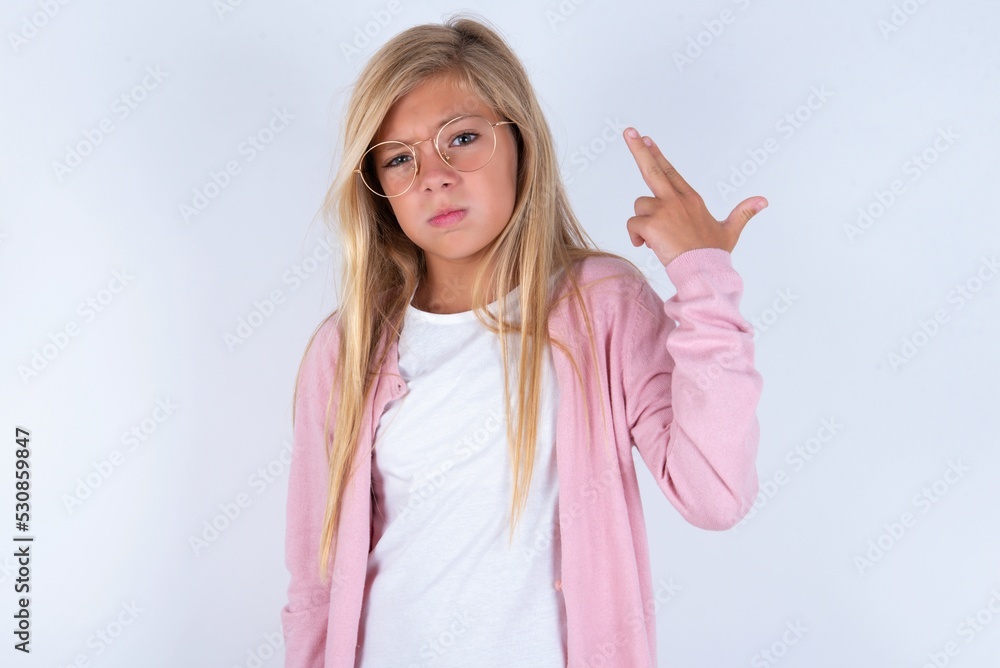 Unhappy caucasian blonde little girl wearing pink jacket and glasses over white background imitates gun shoot makes suicide gesture keeps two fingers on temples. Unhappy caucasian blonde little girl wearing pink jacket and glasses over white background imitates gun shoot makes suicide gesture keeps two fingers on temples.