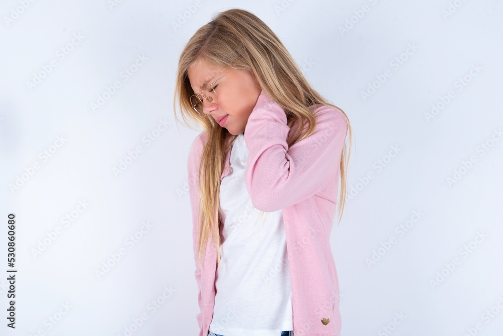 caucasian blonde little girl wearing pink jacket and glasses over white background suffering from back and neck ache injury, touching neck with hand, muscular pain. caucasian blonde little girl wearing pink jacket and glasses over white background suffering from back and neck ache injury, touching neck with hand, muscular pain.
