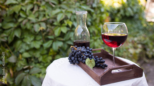 A glass of red wine prepared for tasting stands on a table with a white tablecloth outdoors in sunlight