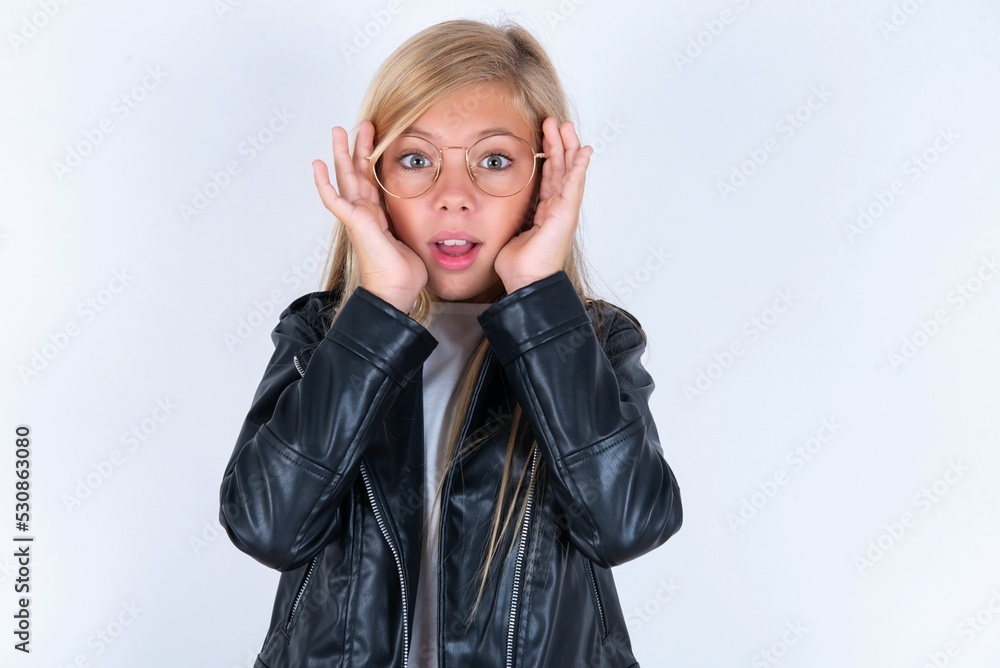 beautiful caucasian blonde little girl wearing biker jacket and glasses over white background Pleasant looking cheerful, Happy reaction beautiful caucasian blonde little girl wearing biker jacket and glasses over white background Pleasant looking cheerful, Happy reaction