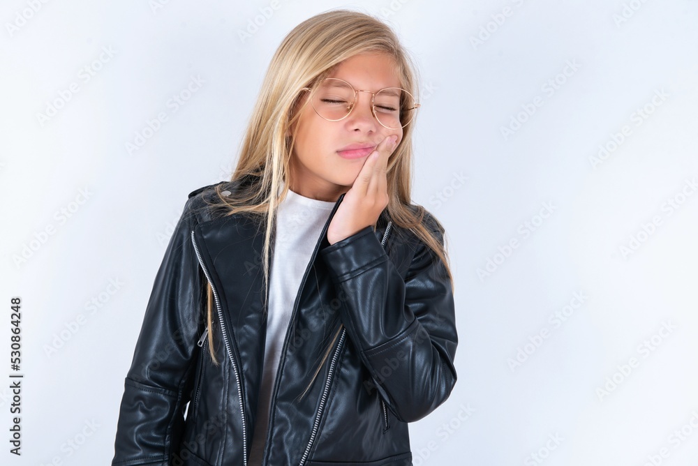 beautiful caucasian blonde little girl wearing biker jacket and glasses over white background with toothache beautiful caucasian blonde little girl wearing biker jacket and glasses over white background with toothache