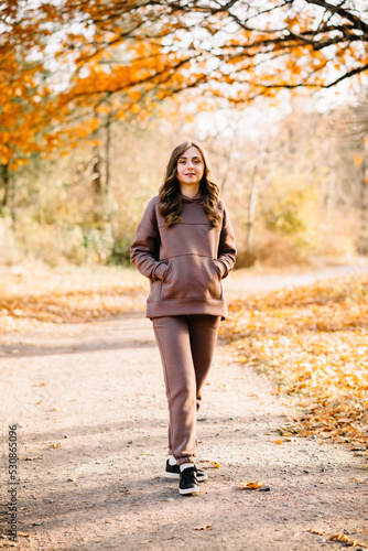 Young woman in hoodie walking in an autumn park. Sunny weather. Fall season.