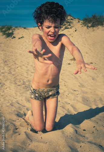 Cute little brunet boy on the beach plays with sand. kids travel concept. Sea holidays, copy space.
