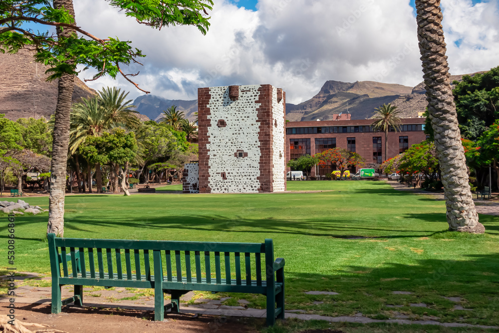 Obraz premium Panoramic view on the tower Torre del conde at the island capital San Sebastian de La Gomera, La Gomera, Canary Islands, Spain, Europe. Bench in the foreground. Tourist attraction in town centre