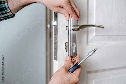 Door lock installation, repair, or replacement service. Door hardware installer locksmith working with open white door indoor photo