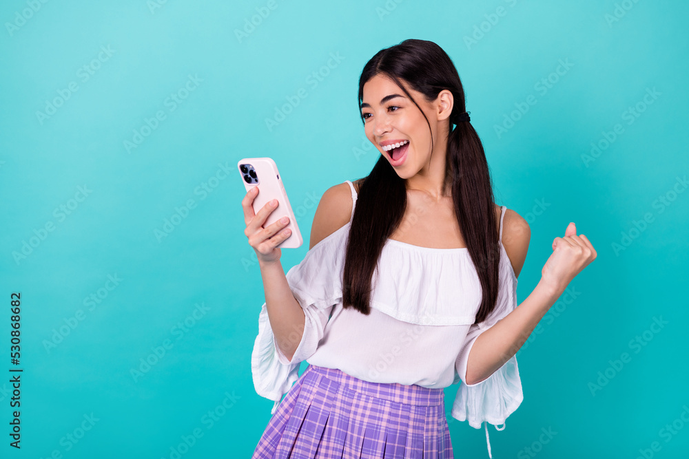 Portrait of excited funny indonesian lady raise fist celebrate achievement hold telephone isolated on teal color background Portrait of excited funny indonesian lady raise fist celebrate achievement hold telephone isolated on teal color background