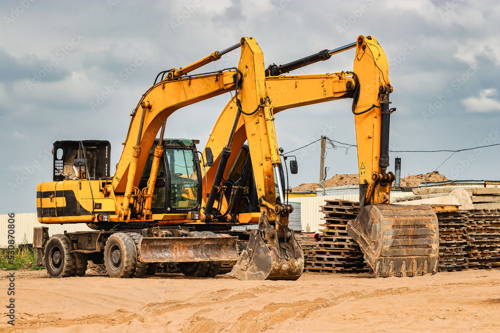 Powerful excavators at a construction site against a blue cloudy sky. Earthmoving construction equipment. Lots of excavators. Powerful excavators at a construction site against a blue cloudy sky. Earthmoving construction equipment. Lots of excavators.