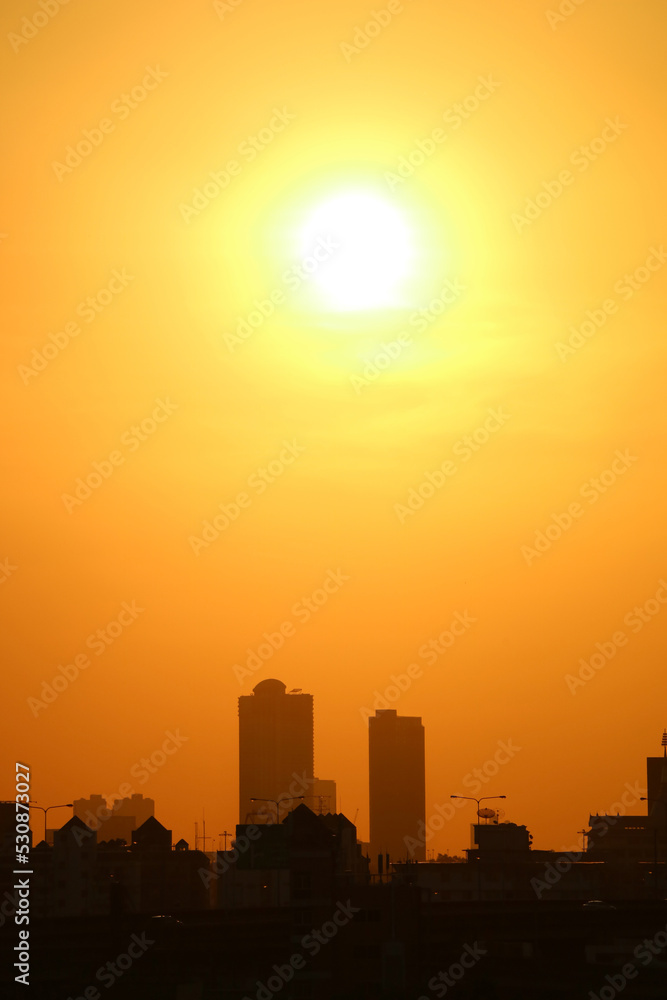 Bright sun shining on vivid orange sky over groups of skyscrapers