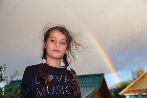 Portrait of a European girl against the sky with a rainbow. You can see the roofs of the houses in the background.