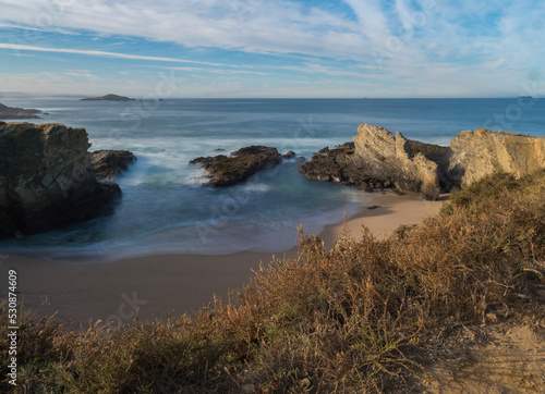 View of empty Praia dos Buizinhos sand beach with long exposure blurred ocean waves and sharp rock and cllifs at wild Vicentina coast in Porto Covo  Portugal. Golden hour.