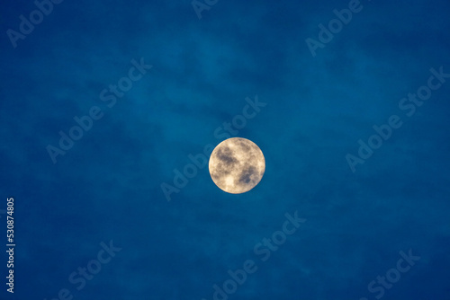 View of an illuminated full moon on a blue sky with dark clouds. © Romar66