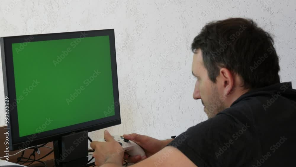 Young male gamer playing game console using joystick remote control over green screen chroma key monitor tv at home. Man Focused Gaming in Living Room Young male gamer playing game console using joystick remote control over green screen chroma key monitor tv at home. Man Focused Gaming in Living Room