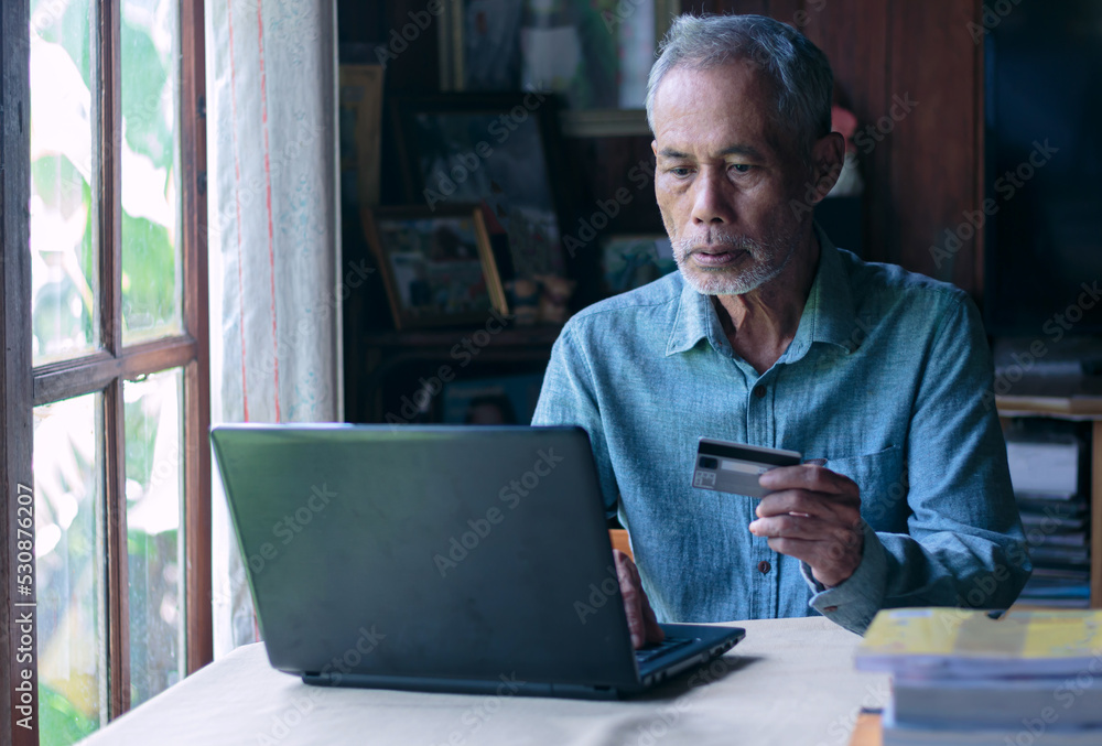 Asian old man using laptop and credit card payment online shopping by connecting customer network through omni channel old man with technology Asian old man using laptop and credit card payment online shopping by connecting customer network through omni channel old man with technology