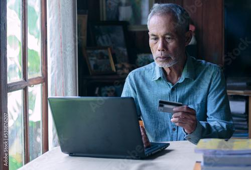 Asian old man using laptop and credit card payment online shopping by connecting customer network through omni channel old man with technology